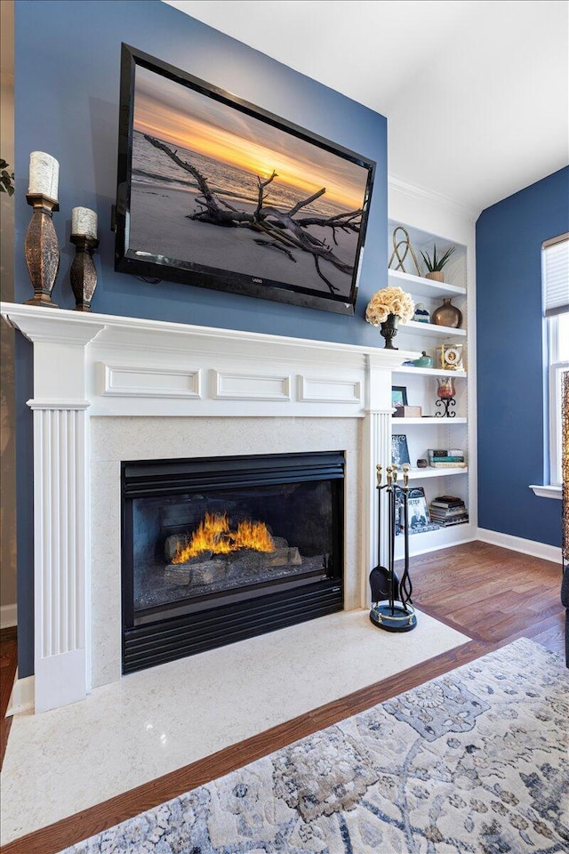 interior details with baseboards, wood finished floors, a glass covered fireplace, and built in features