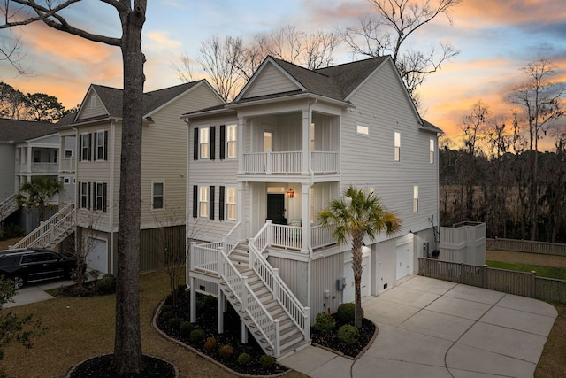 view of front of property with an attached garage, a balcony, covered porch, concrete driveway, and stairway