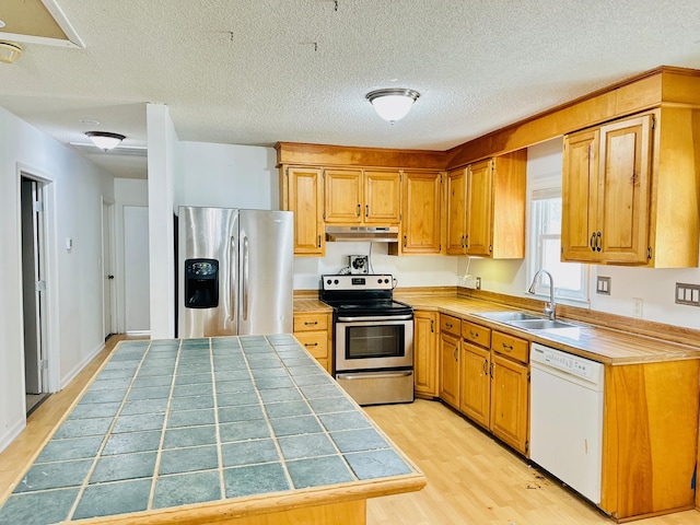 kitchen with a textured ceiling, stainless steel appliances, sink, tile countertops, and light hardwood / wood-style flooring