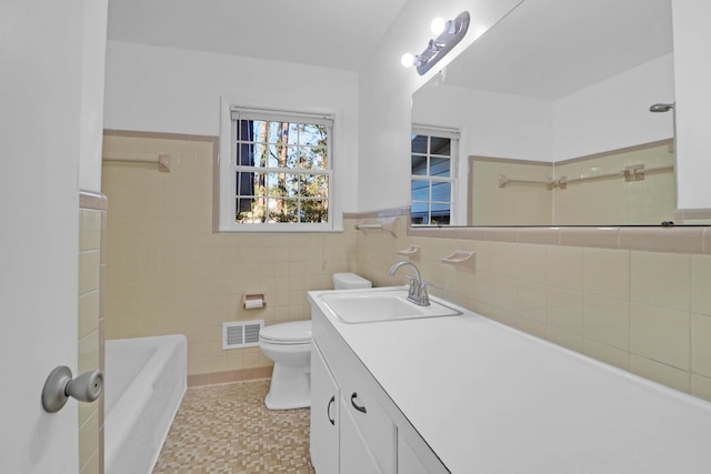 full bathroom with visible vents, tile walls, toilet, a bathing tub, and vanity