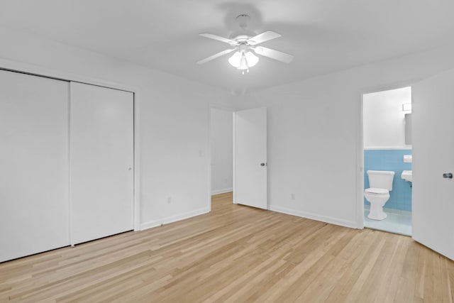 unfurnished bedroom featuring tile walls, wood finished floors, a closet, and ensuite bathroom