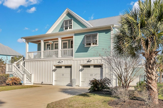 raised beach house with stairs, a garage, concrete driveway, and covered porch