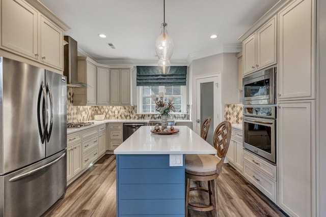 kitchen featuring light countertops, crown molding, decorative backsplash, wall chimney range hood, and appliances with stainless steel finishes