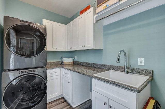 laundry room featuring wood finished floors, stacked washer and clothes dryer, cabinet space, and a sink