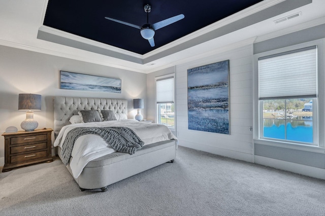 carpeted bedroom with a ceiling fan, a raised ceiling, ornamental molding, and visible vents