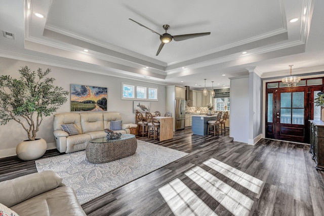 living room featuring a raised ceiling, ceiling fan with notable chandelier, and dark wood-type flooring