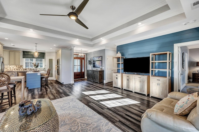 living room featuring dark wood-type flooring, crown molding, ceiling fan with notable chandelier, and a raised ceiling