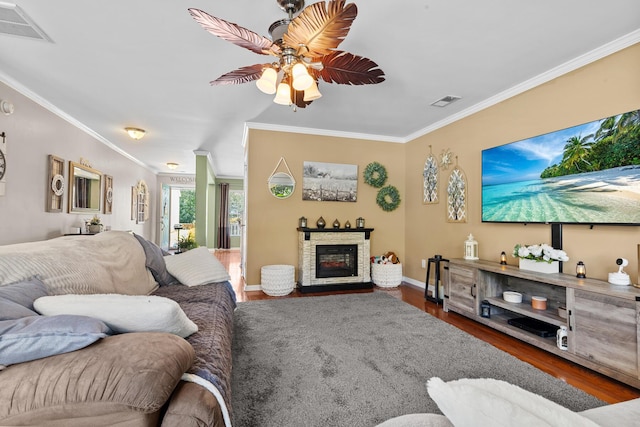 living area with ornamental molding, a ceiling fan, wood finished floors, a fireplace, and baseboards