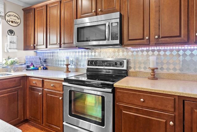 kitchen with appliances with stainless steel finishes, crown molding, decorative backsplash, and brown cabinets