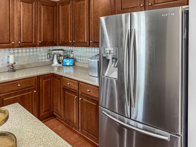 kitchen featuring stainless steel fridge, light wood-style flooring, decorative backsplash, and brown cabinetry