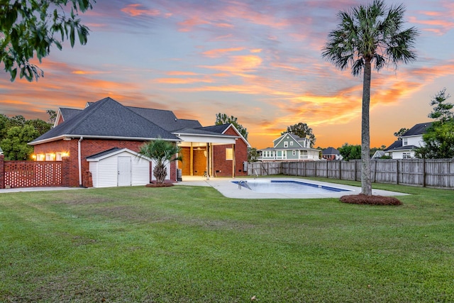 pool at dusk featuring a storage shed and a yard