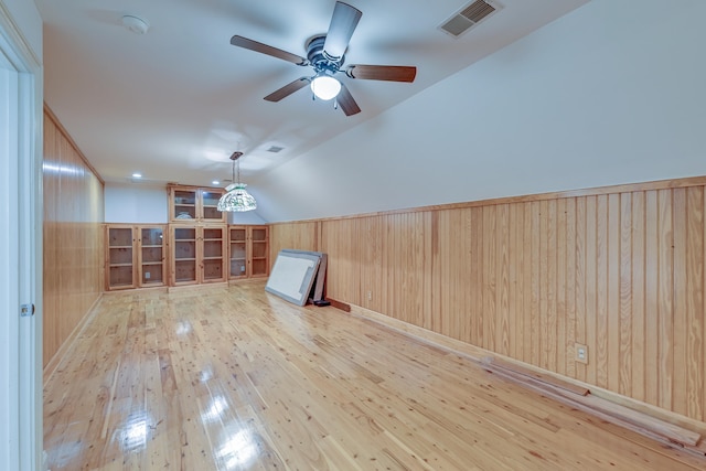 additional living space with lofted ceiling, light hardwood / wood-style flooring, wood walls, and ceiling fan