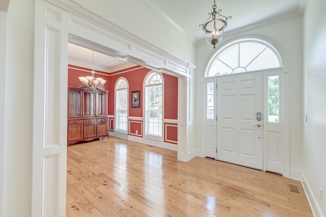 foyer featuring light wood-type flooring, ornamental molding, and an inviting chandelier