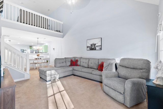 living area featuring ceiling fan with notable chandelier, stairway, carpet floors, a high ceiling, and baseboards