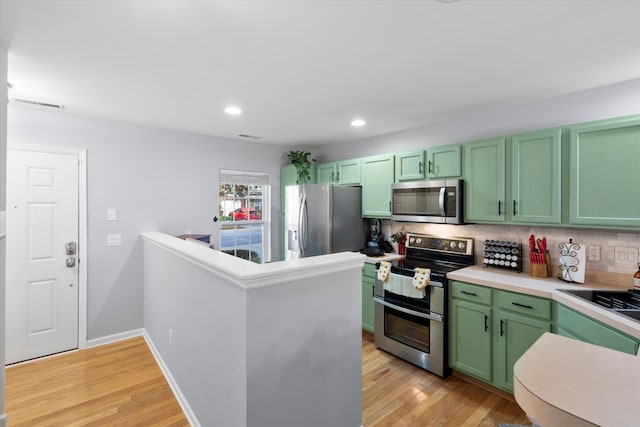 kitchen featuring stainless steel appliances, light wood-style floors, green cabinets, and decorative backsplash