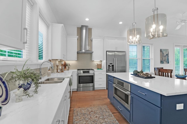 kitchen with appliances with stainless steel finishes, a center island, white cabinets, blue cabinets, and wall chimney exhaust hood