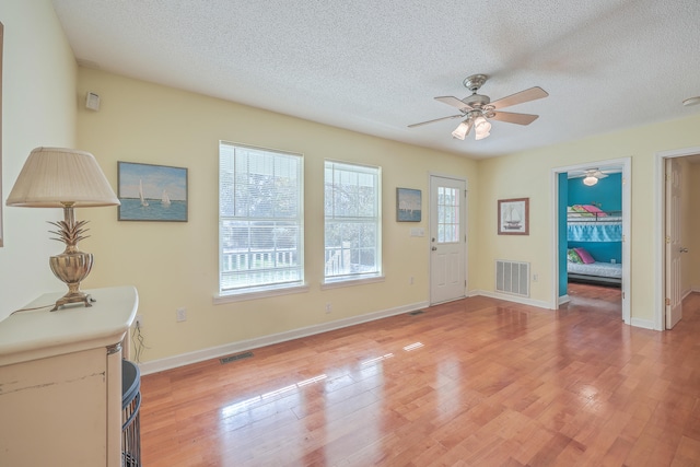 foyer entrance with ceiling fan, light hardwood / wood-style floors, and a textured ceiling