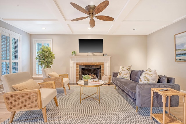 living room featuring ceiling fan, coffered ceiling, a brick fireplace, light wood finished floors, and crown molding