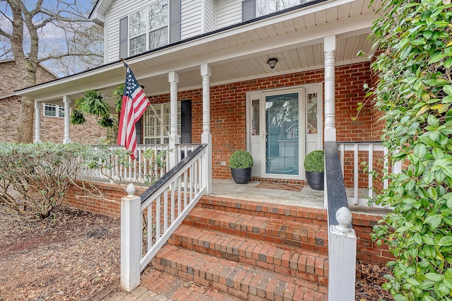 doorway to property with a porch and brick siding