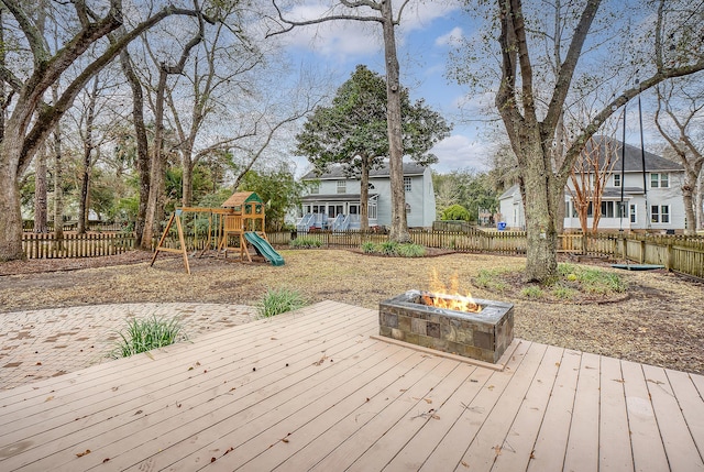 deck with an outdoor fire pit, a playground, and a fenced backyard