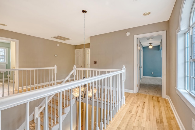 hall with baseboards, visible vents, light wood finished floors, and an upstairs landing