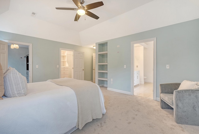 bedroom featuring light carpet, baseboards, lofted ceiling, ensuite bathroom, and a walk in closet