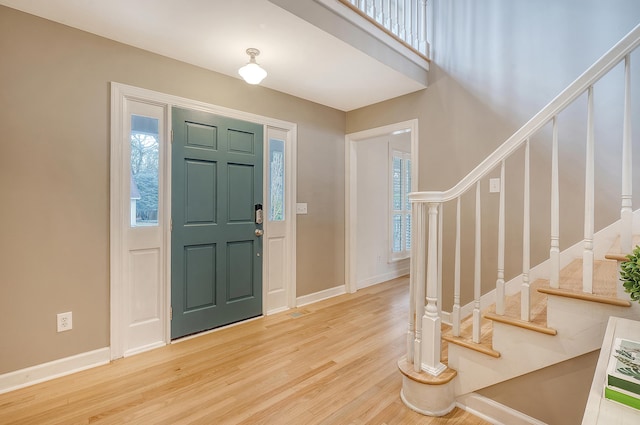 foyer entrance featuring light wood finished floors, baseboards, visible vents, and stairway