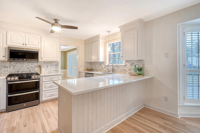 kitchen featuring a sink, stainless steel appliances, hanging light fixtures, and light countertops