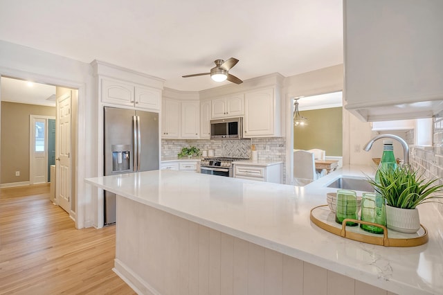 kitchen with tasteful backsplash, a peninsula, stainless steel appliances, white cabinetry, and a sink