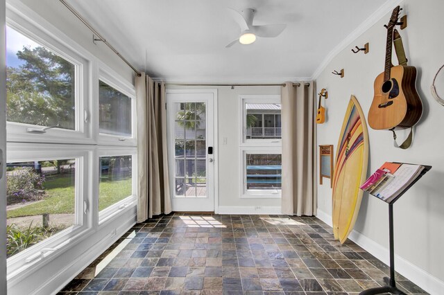 interior space with ceiling fan, a wealth of natural light, dark tile patterned floors, and crown molding