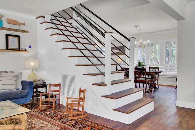 staircase with crown molding, hardwood / wood-style flooring, and a notable chandelier