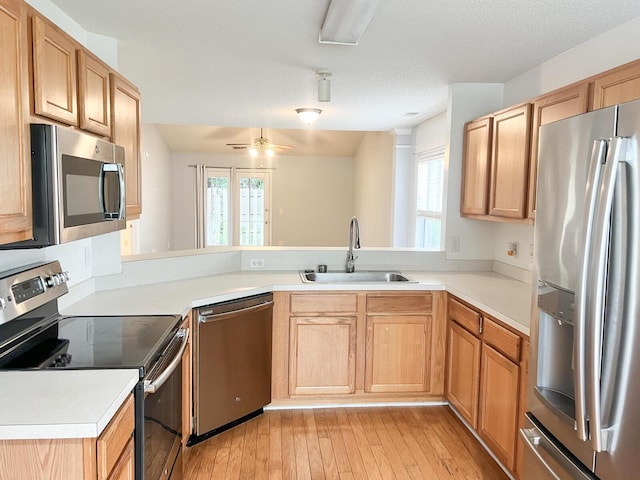 kitchen featuring appliances with stainless steel finishes, a sink, light wood-style floors, and a peninsula