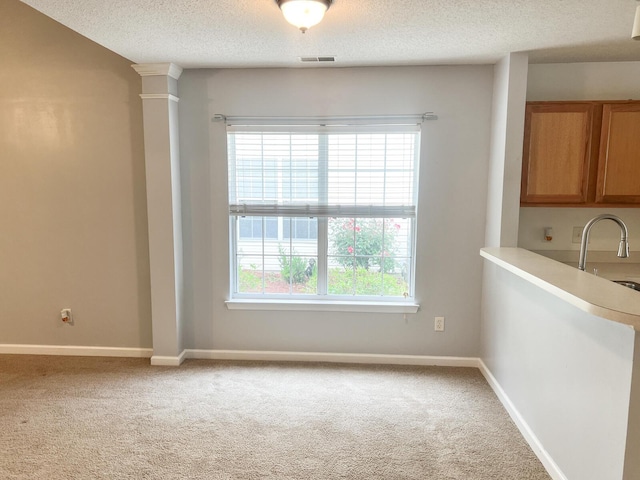 unfurnished dining area featuring light colored carpet, a textured ceiling, baseboards, and decorative columns