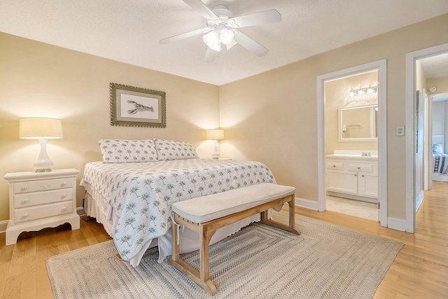 bedroom featuring baseboards, light wood-style floors, ensuite bath, and a ceiling fan