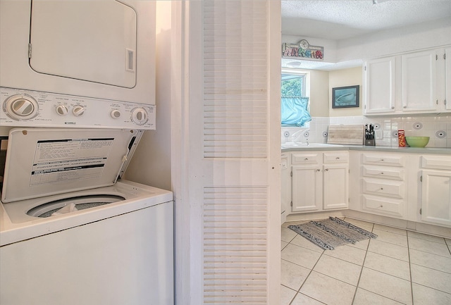 laundry area with light tile patterned floors, a textured ceiling, laundry area, and stacked washer / dryer