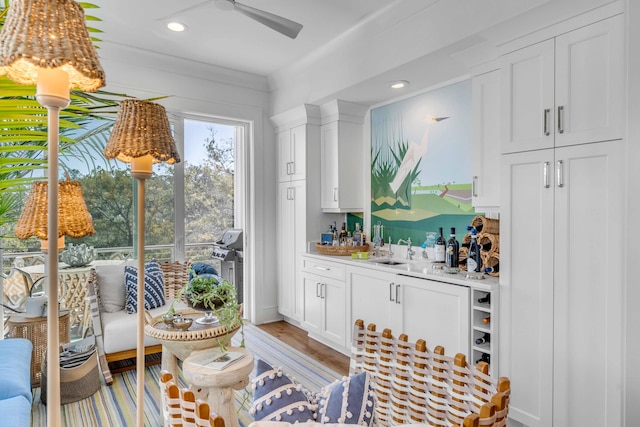 bar featuring light hardwood / wood-style floors, white cabinets, ceiling fan, ornamental molding, and sink