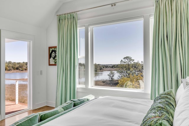 bedroom featuring wood-type flooring, lofted ceiling, multiple windows, and a water view