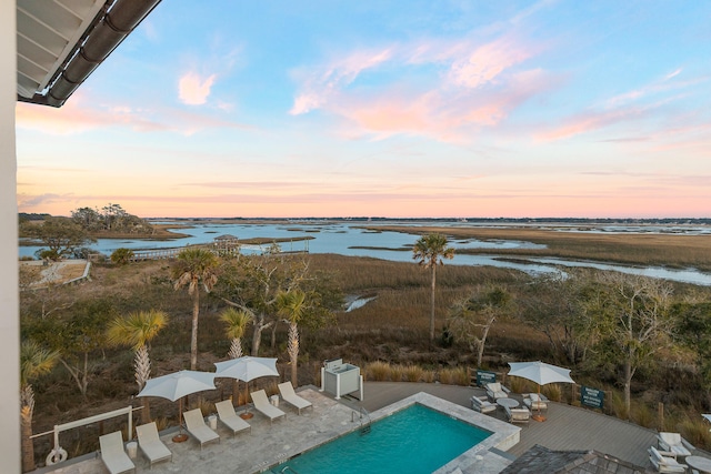 pool at dusk featuring a grill, a water view, and a patio area