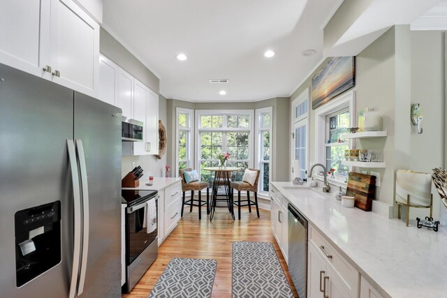 kitchen featuring stainless steel appliances, sink, white cabinetry, light wood-type flooring, and a healthy amount of sunlight