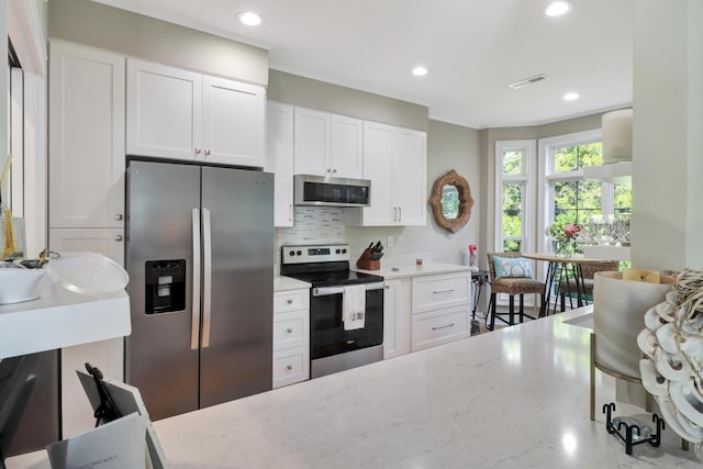 kitchen with light stone countertops, white cabinetry, appliances with stainless steel finishes, and decorative backsplash