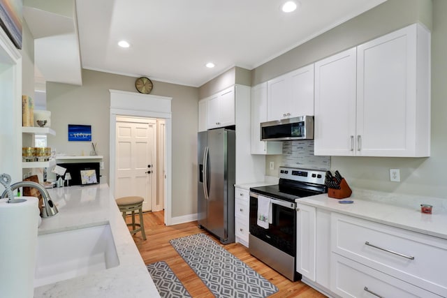 kitchen featuring appliances with stainless steel finishes, white cabinetry, sink, light stone countertops, and light hardwood / wood-style flooring