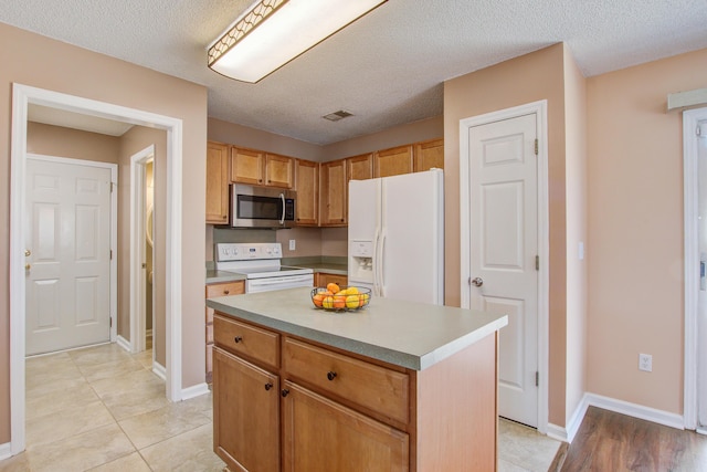 kitchen featuring white appliances, baseboards, visible vents, a center island, and light countertops