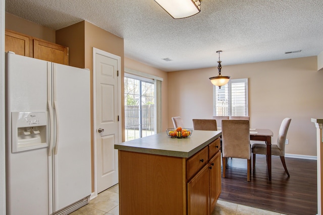 kitchen featuring white fridge with ice dispenser, a center island, a healthy amount of sunlight, and hanging light fixtures