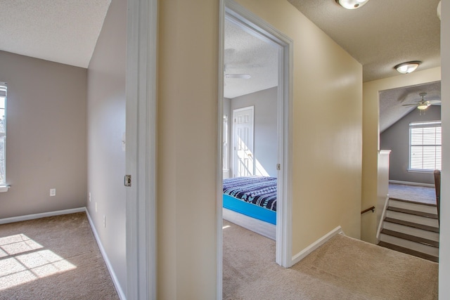 corridor with carpet, baseboards, a textured ceiling, and an upstairs landing