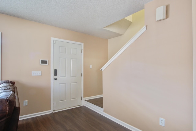 foyer entrance with a textured ceiling, dark wood-type flooring, stairs, and baseboards