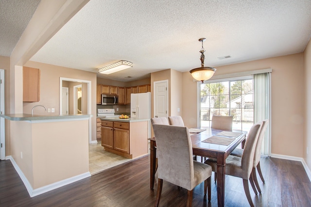 dining area with dark wood-style floors, visible vents, a textured ceiling, and baseboards