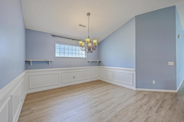 empty room with a chandelier, a textured ceiling, and wood finished floors