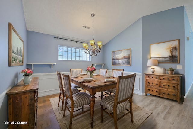 dining space featuring visible vents, lofted ceiling, light wood-style floors, wainscoting, and a notable chandelier