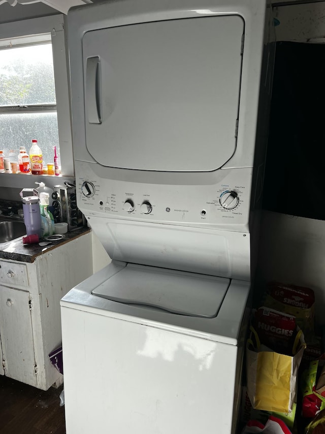 clothes washing area with dark wood finished floors, laundry area, and stacked washing maching and dryer