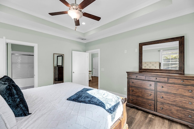 bedroom with a raised ceiling, ceiling fan, dark hardwood / wood-style flooring, and connected bathroom